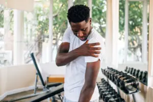 man standing and suffering from shoulder pain during workout with dumbbells