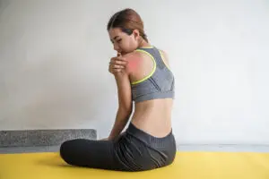 Woman with shoulder pain on yellow yoga mat