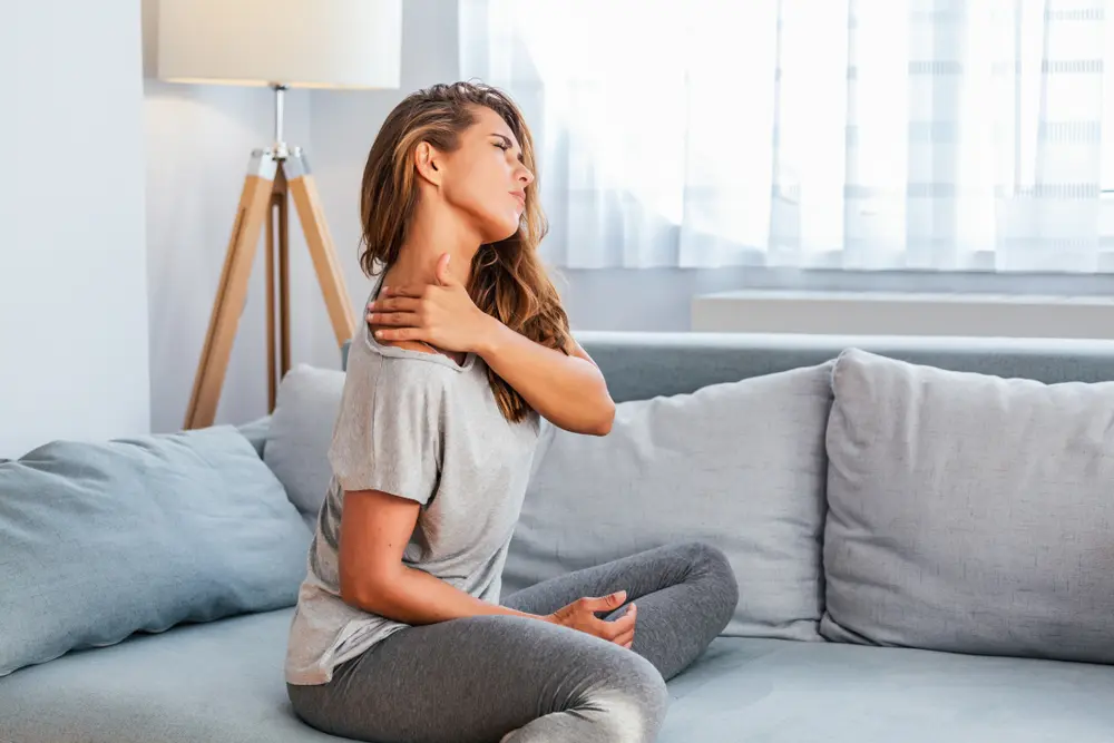 woman sitting on the bed and holding painful shoulder with another hand.