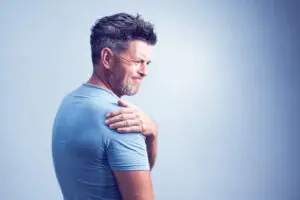 middle aged man experiencing shoulder pain on grey background