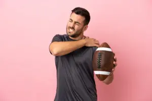 Young caucasian man playing rugby isolated on pink background suffering from pain in shoulder.